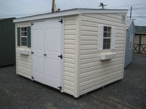Vinyl lean to shed delivered to Maryland with vinyl siding and white shutters and white flower boxes. This storage shed has white steel doors.
