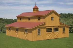 Two story modular horse barn built with natural pine board and batten, center aisle is open with stalls on either side, hay storage area in loft space of horse barn. custom cupola is on roof.
